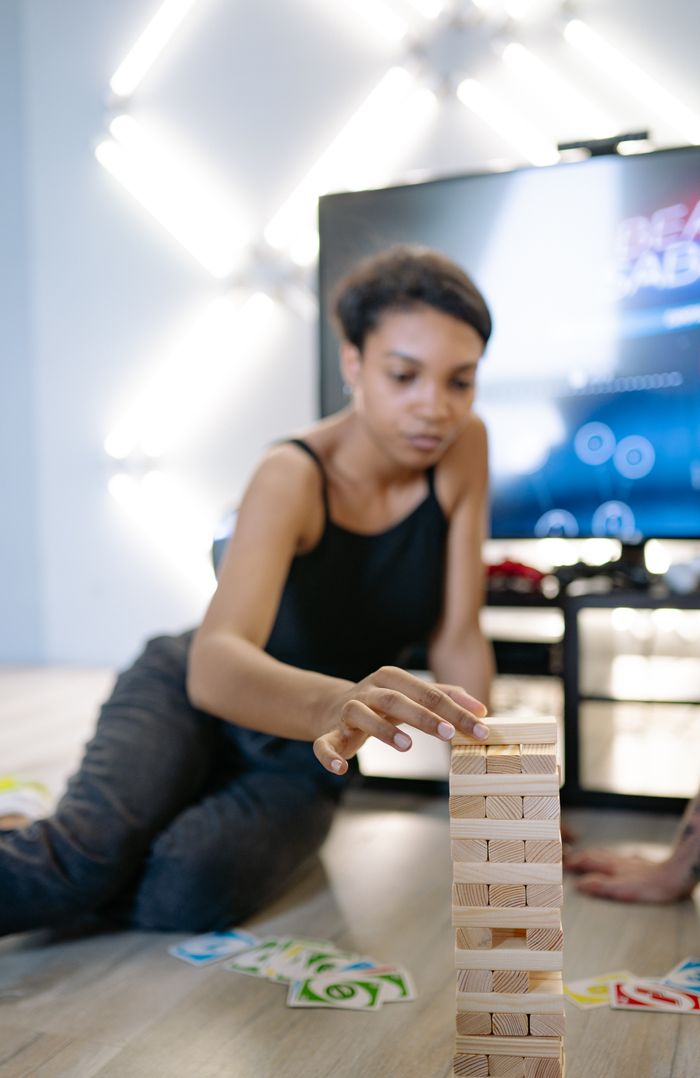 A young woman carefully pulls a block from a Jenga tower, playing indoors.